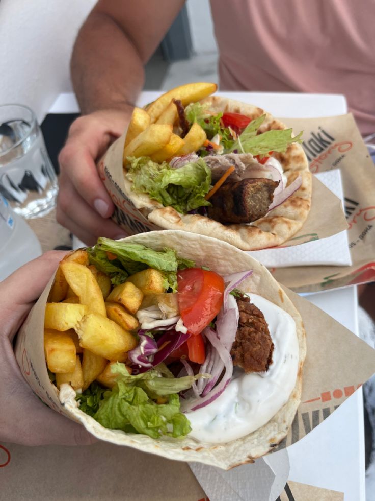 two tacos with meat, lettuce and fruit on them are being held by people