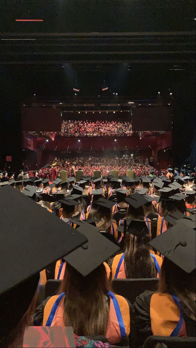 a large group of people in graduation caps and gowns sitting on stage with an audience