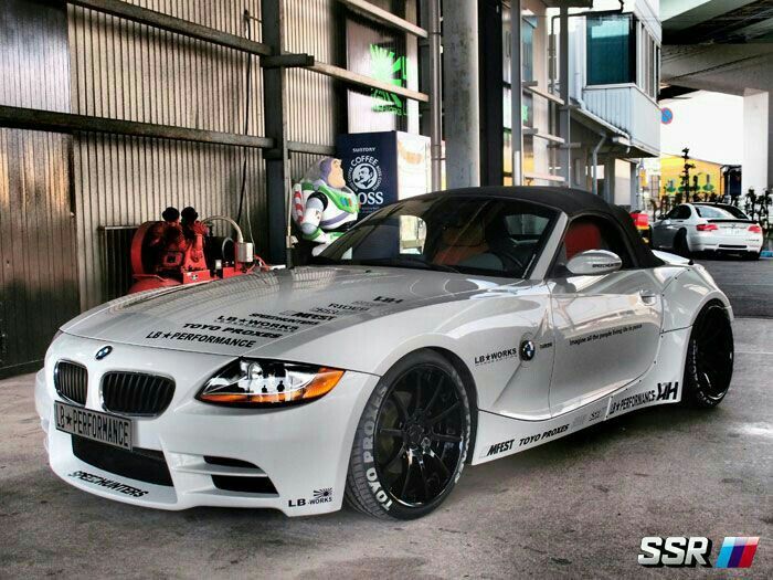 a white bmw z4 parked in front of a building with other cars behind it