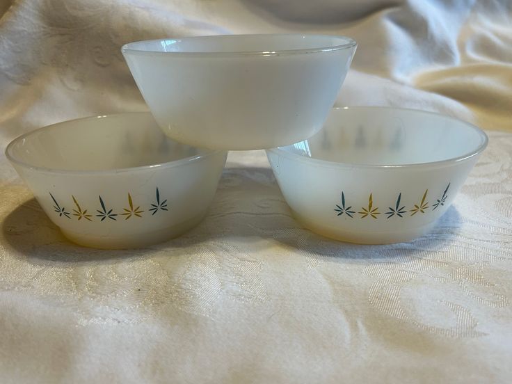 three white bowls sitting next to each other on top of a tablecloth covered bed