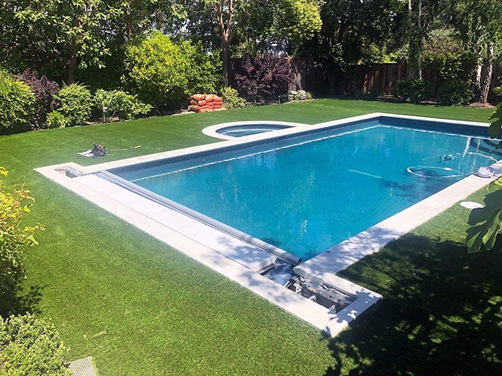 an empty swimming pool in the middle of a lush green yard with trees and bushes