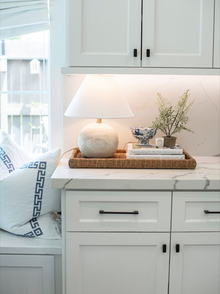 a kitchen with white cabinets and a basket on the counter top next to a window