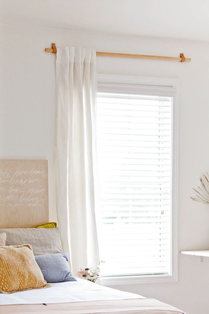 a white bed sitting next to a window in a room with curtains on the windowsill