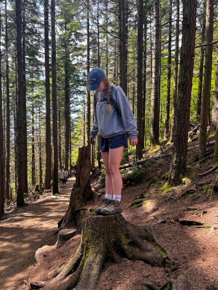 a woman standing on top of a tree stump in the woods with her back to the camera