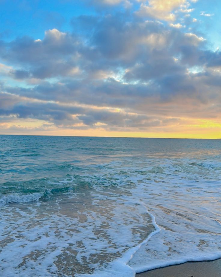 the ocean waves come in to shore as the sun is setting over the water and clouds