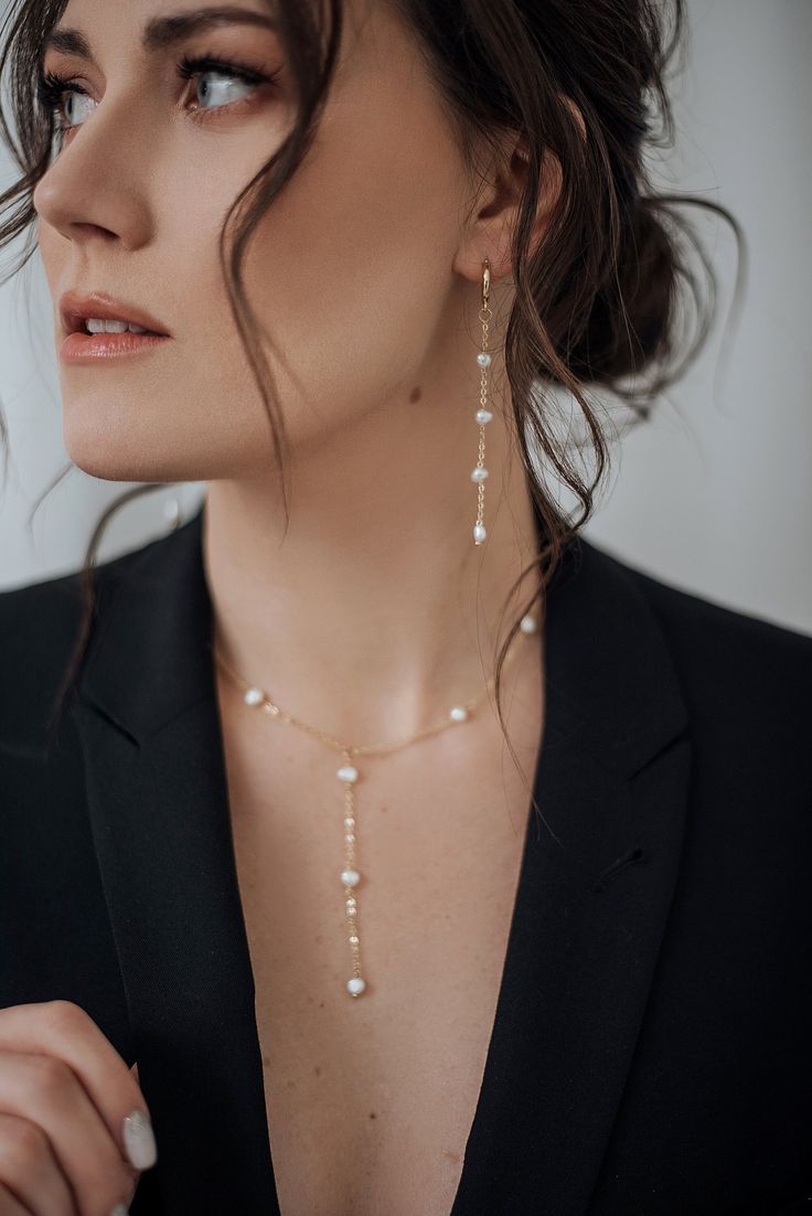 a woman in a black suit and white pearls is wearing a necklace that has been attached to her neck