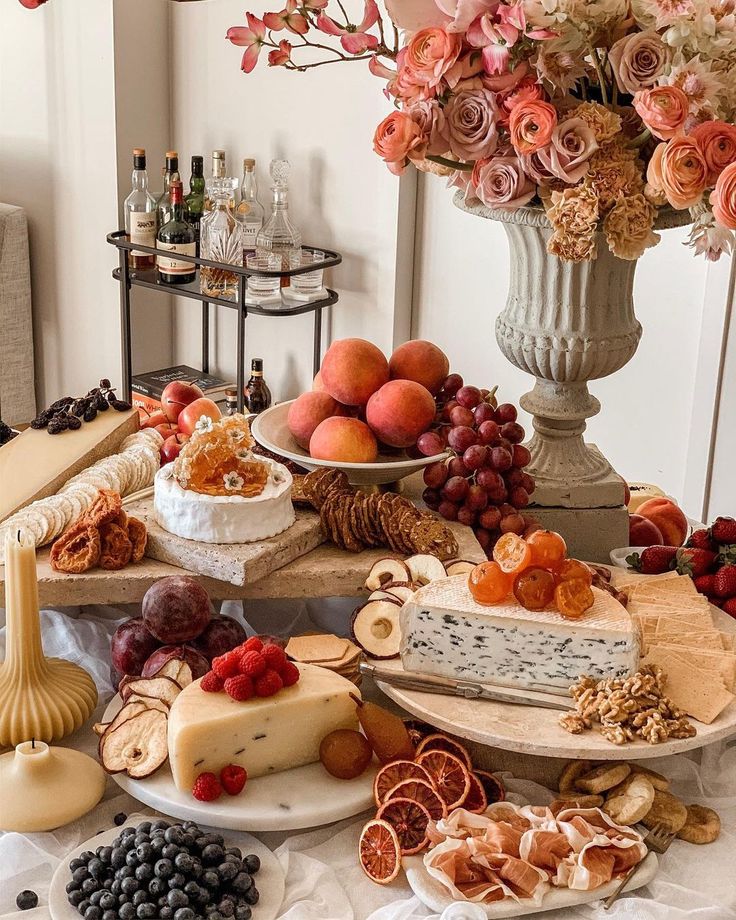 a table topped with lots of different types of cheeses and fruit next to a vase filled with flowers