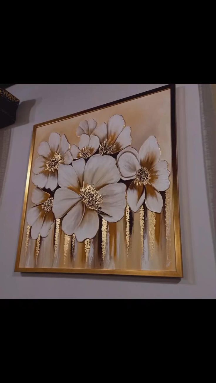 a painting hanging on the side of a wall with flowers in gold and white colors