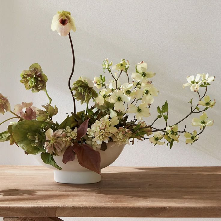 a white vase filled with flowers on top of a wooden table