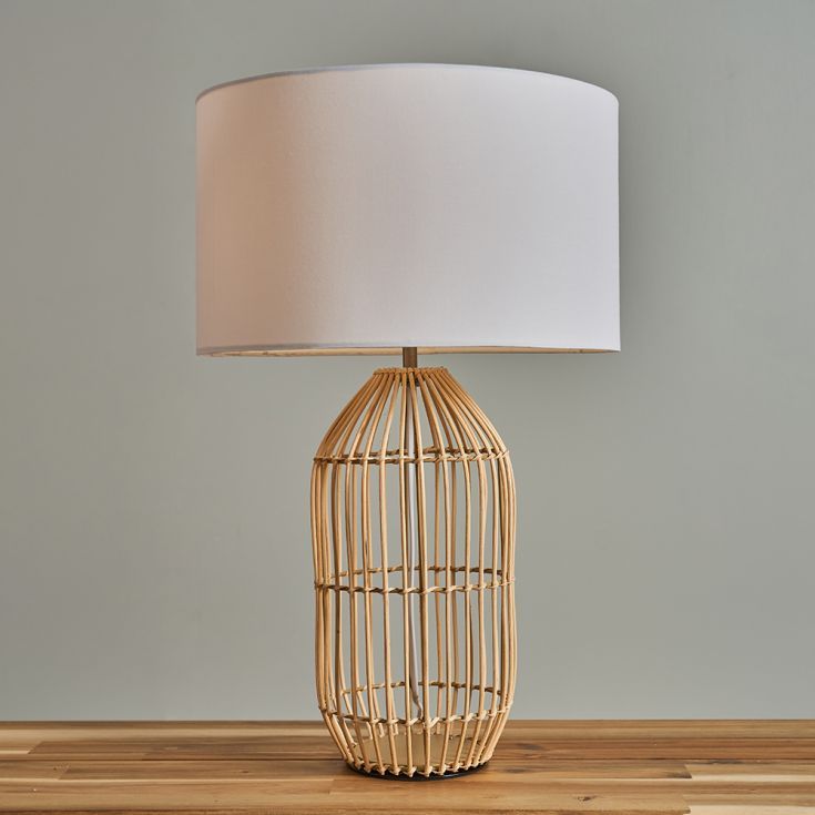 a table lamp with a white shade on it sitting on a wooden table next to a gray wall