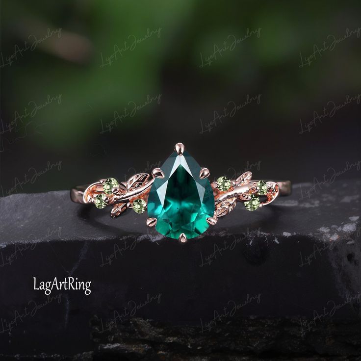 an emerald colored ring with green and white stones on it's sides, sitting on top of a rock