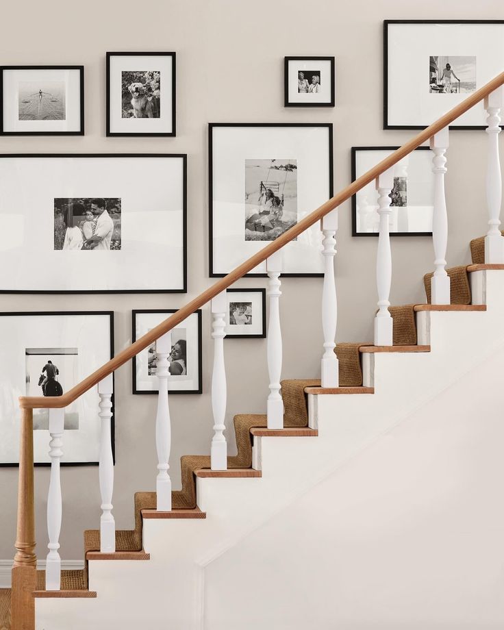 a stair case with pictures on the wall and framed photos above it, along with a wooden handrail