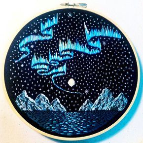 an embroidery project with blue and white lights in the night sky over water, mountains and stars