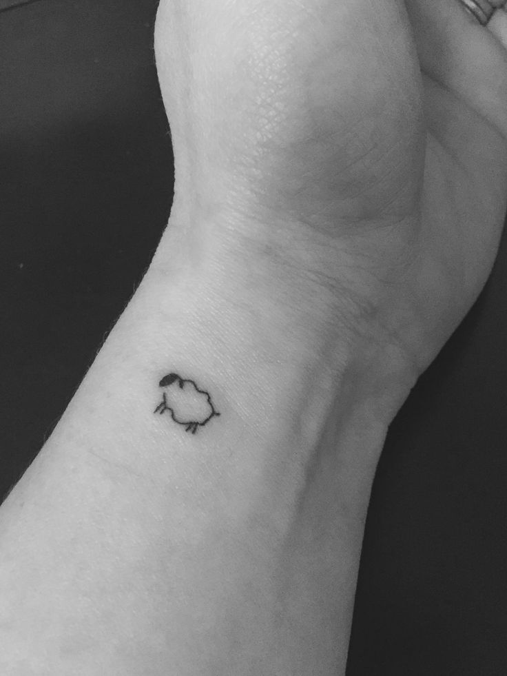 a black and white photo of a person's wrist with a small sheep tattoo on it