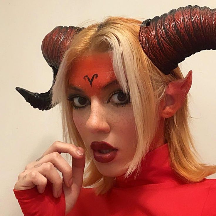 a woman with horns on her head is posing for the camera while wearing red makeup