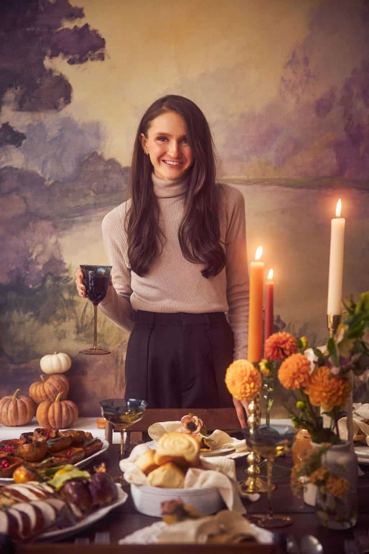 a woman standing in front of a table filled with food and candles, holding a cup