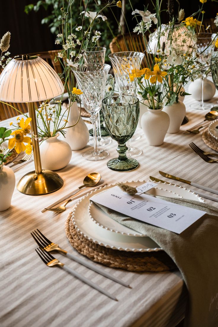 the table is set with silverware and yellow flowers in glass vases, along with other place settings