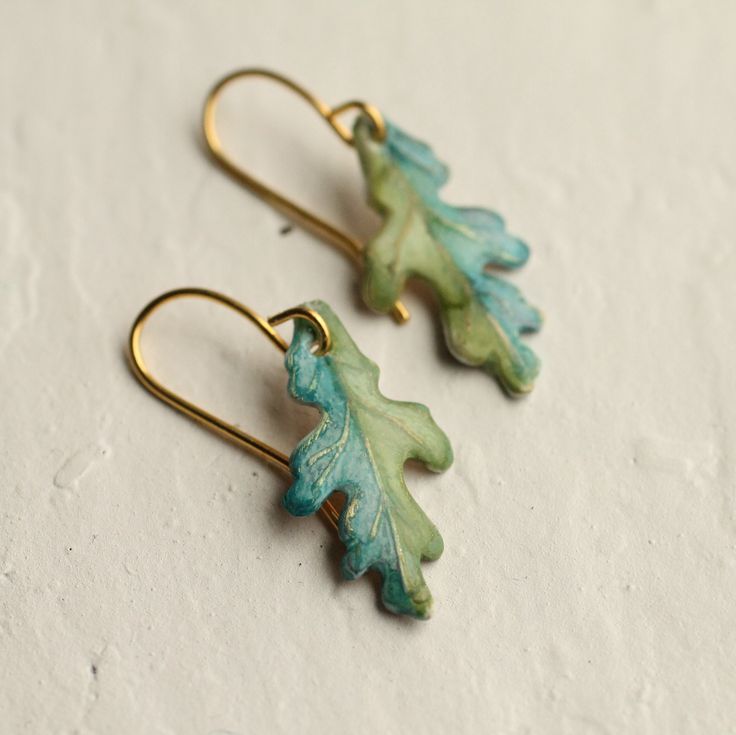 two green leaf shaped earrings sitting on top of a white table next to each other