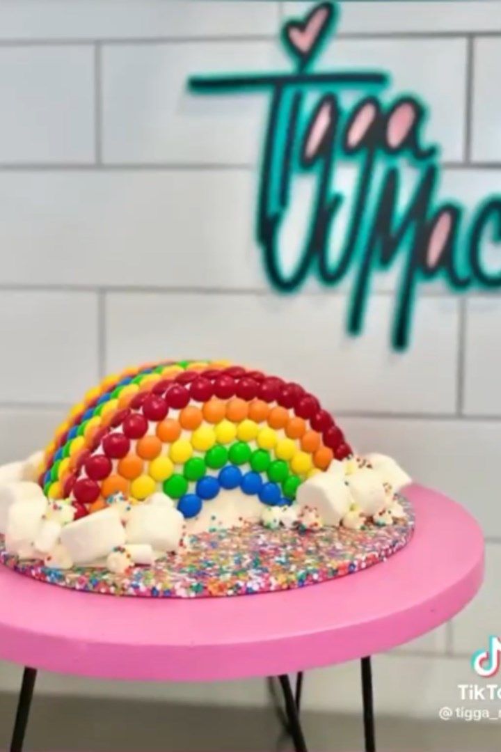 a rainbow cake on a pink table in front of a sign that says tempie