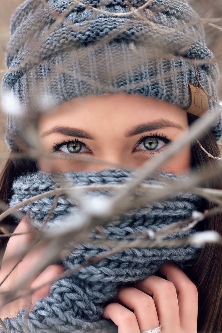 a woman wearing a gray knitted hat and scarf with her hands under her face