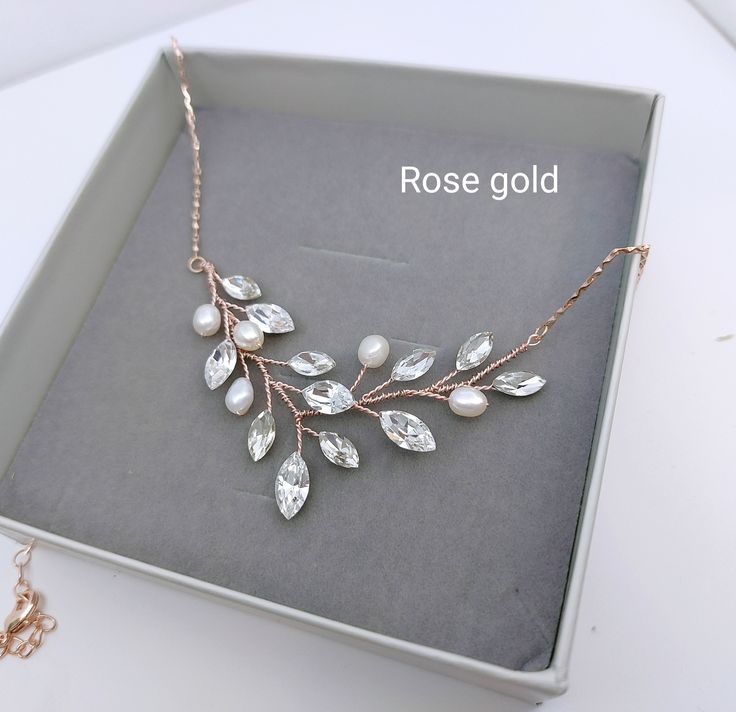 a rose gold necklace with white pearls and leaves on it in a box next to a chain