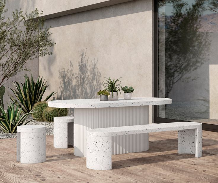 a white table and benches in front of a building with potted plants on it