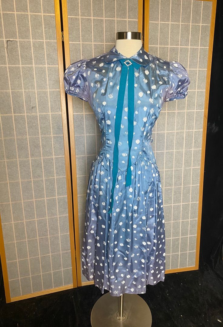 Late 1940's/early 50's blue satin dress with white polka dots, puffy sleeves, and blue neck ribbon with rhinestone brooch. This dress is wearable but in only fair condition. Both underarms have fading and staining and small rips. Lots of the white polka dots are rubbing off and missing the 'paint.' Missing the original belt. Metal zipper up the back. See all photos, being sold as is Women's medium Measurements coming Elegant Blue Vintage Dress For Vintage Events, Blue Vintage Dress For Vintage Events, Blue Fitted Vintage Dress For Vintage Occasions, Retro Blue Dress For Vintage Events, Retro Blue Dresses For Vintage Events, Blue Vintage Summer Dress For Formal Occasions, Blue Vintage Dress For Summer Formal, Blue Formal Dress In 1950s Style, Summer Vintage Blue Formal Dress