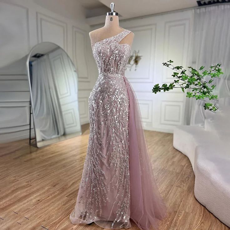 Exquisite mermaid silhouette gown in a lovely pink hue, perfect for elegant occasions. Crafted with meticulous attention to detail and high-quality materials for a luxurious feel. Features an elegant one-shoulder design for a sophisticated look. Adorned with luxurious beadwork for added glamour and opulence. Designed with an overskirt that adds a touch of elegance and drama. Ideal attire for women attending weddings, formal events, or parties. Elevate your ensemble with this stunning gown, epito Glamorous Pink Mermaid Dress For Banquet, Pink Floor-length Gown For Banquet, Pink Floor-length Banquet Gown, Pink Mermaid Dress With Fitted Bodice For Banquet, Pink Gown With Sweep Train For Banquet, Pink Mermaid Fishtail Dress For Banquet, Pink Fishtail Mermaid Dress For Banquet, Pink Fishtail Banquet Dress, Fitted Pink Mermaid Dress For Banquet