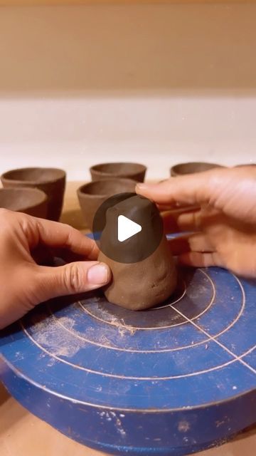 two hands are holding clay cups on a blue board with holes in the middle, while another hand holds one