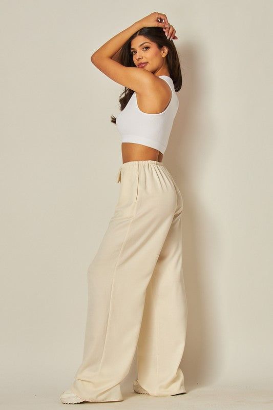 Elevate your wardrobe with our Ivory Satin Wide Leg Pants. Featuring a stylish tie waist drawstring, wide leg design, and convenient side pockets, these pants offer both comfort and sophistication. Upgrade your look with this versatile and chic fashion essential. Fabric & fit: Model is wearing size Small. Wide Leg Pants With Tie Waist For Loungewear, Loungewear Wide Leg Pants With Tie Waist, Chic Cream Wide Leg Pants For Loungewear, Chic Beige Wide Leg Pants With Tie Waist, Chic Tie Waist Loungewear Bottoms, Chic Tie Waist Bottoms For Loungewear, Chic Loungewear Bottoms With Tie Waist, Wide Leg High-waisted Pants With Tie Waist For Loungewear, Chic Loungewear Pants With Tie Waist