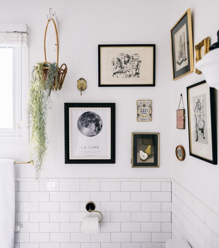 a white bathroom with pictures and other items on the wall above the toilet, along with plants