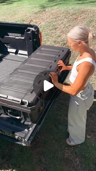 a woman standing in front of a black truck with the hood open and it's cargo compartment opened