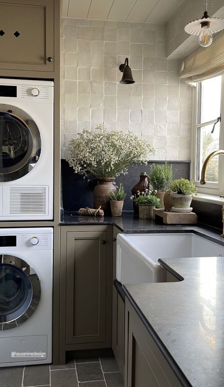 a washer and dryer sitting in a kitchen next to a window with potted plants