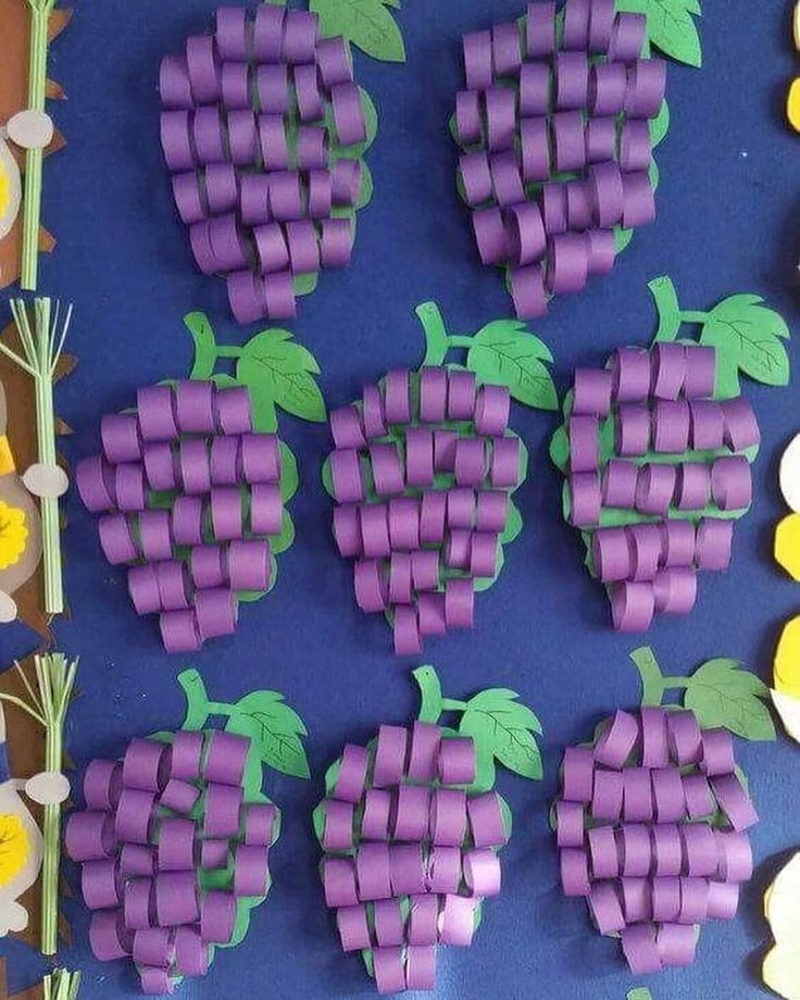 grapes made out of toilet paper sitting on top of a blue surface next to flowers