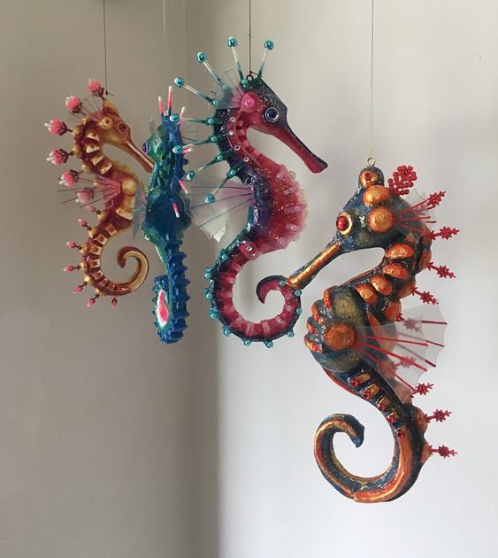 three seahorses are hanging from the ceiling and one is painted red, blue, and green