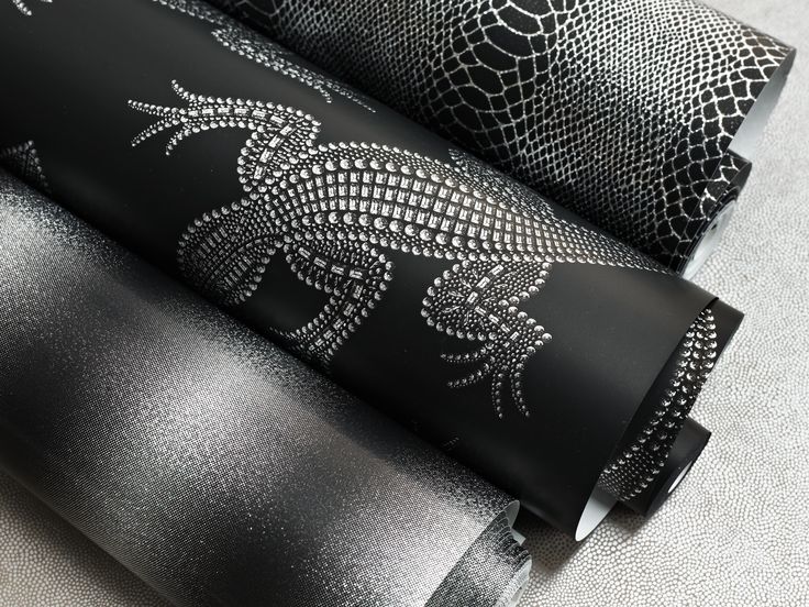 two rolls of black and white fabric with silver designs on them, one rolled up to the side