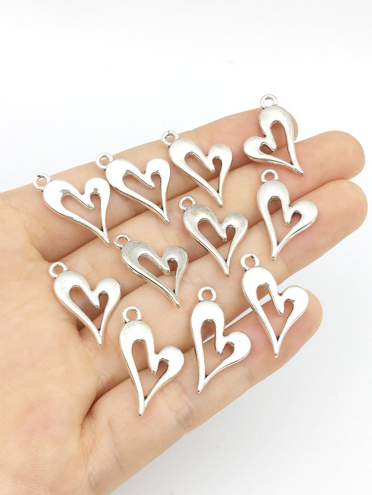 small silver heart charms in the shape of hearts on a person's hand with white background