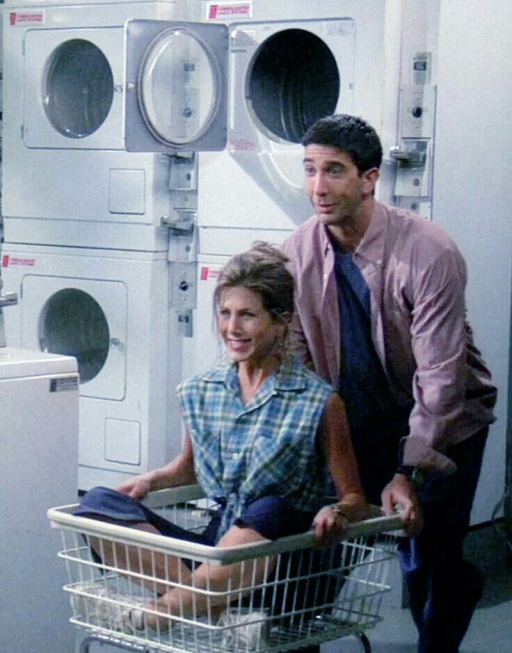 a man and woman sitting in a laundry basket next to a washer dryer