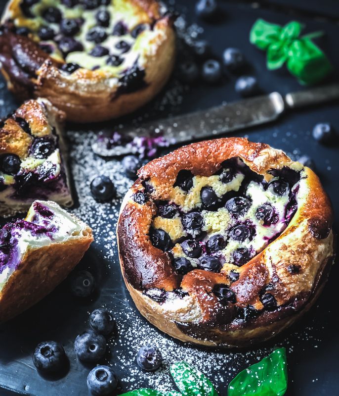 blueberry cheesecakes with fresh blueberries and mint leaves on a black surface