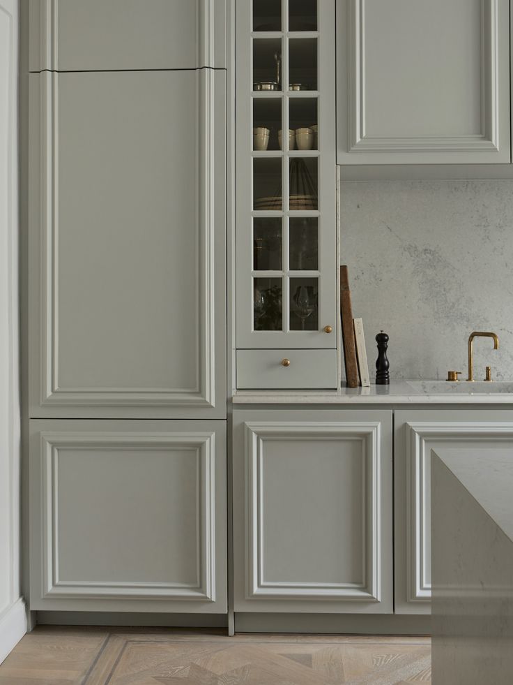 a kitchen with gray cabinets and marble counter tops, along with a white sink in the center