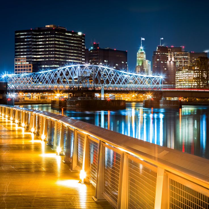 the city skyline is lit up at night with lights reflecting on the water and bridge