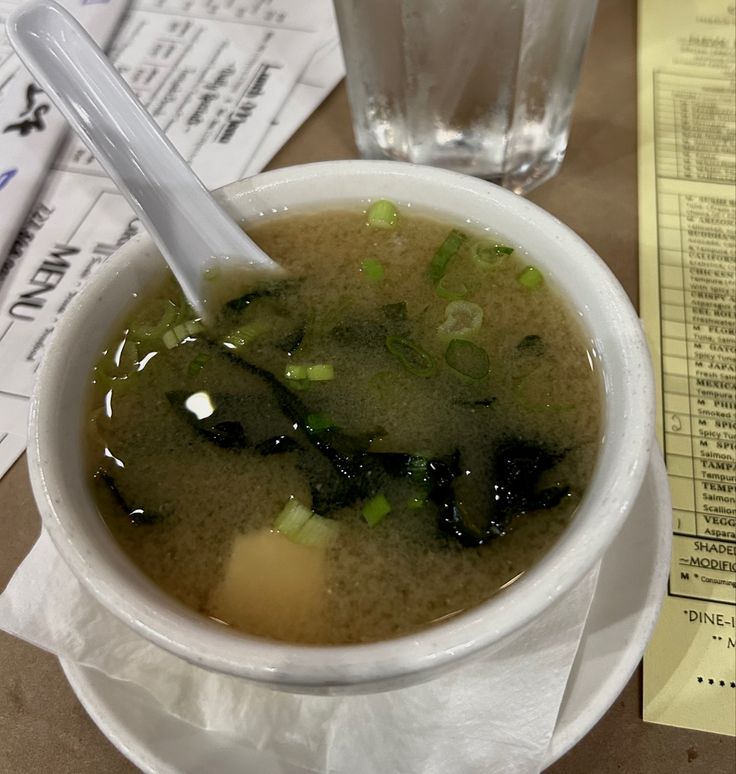 a white bowl filled with soup next to a cup of water and papers on a table