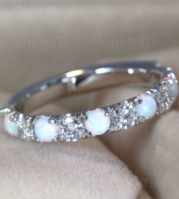 a white opal and diamond ring sitting on top of a pillow