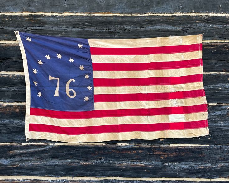 an old american flag hanging on the side of a wooden building with numbers 76 written on it