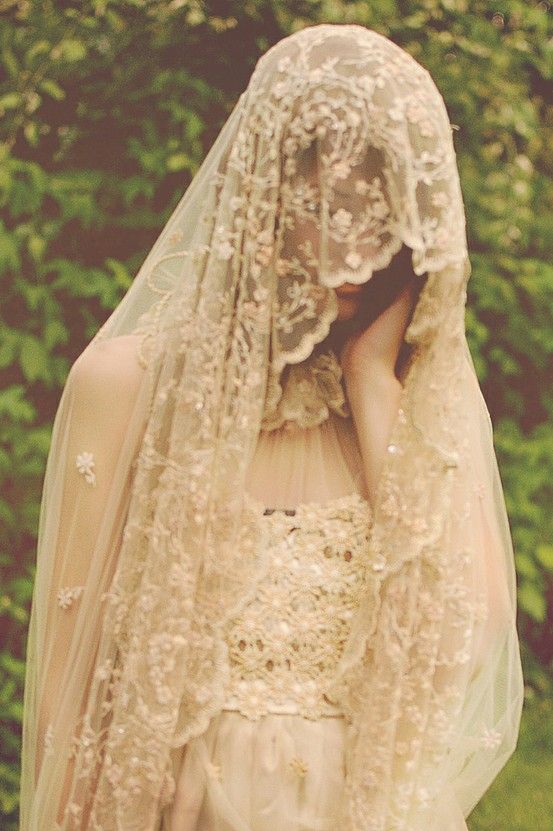 a woman wearing a veil and dress with flowers on it's head is standing in front of some trees