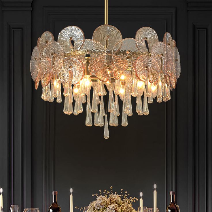 a chandelier hanging over a dining room table with wine glasses and plates on it