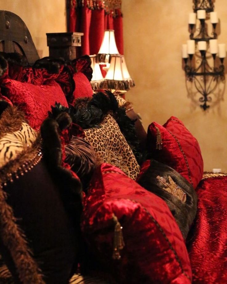 a bed covered in red and leopard print pillows next to a chandelier with two lamps on either side