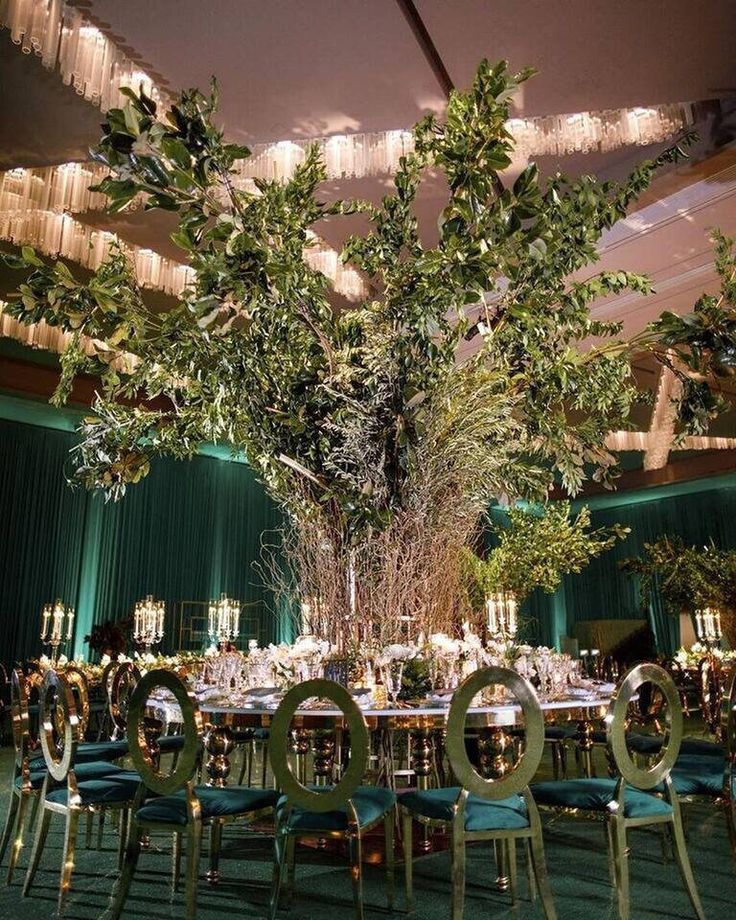 a table set up for an event with green chairs and greenery hanging from the ceiling