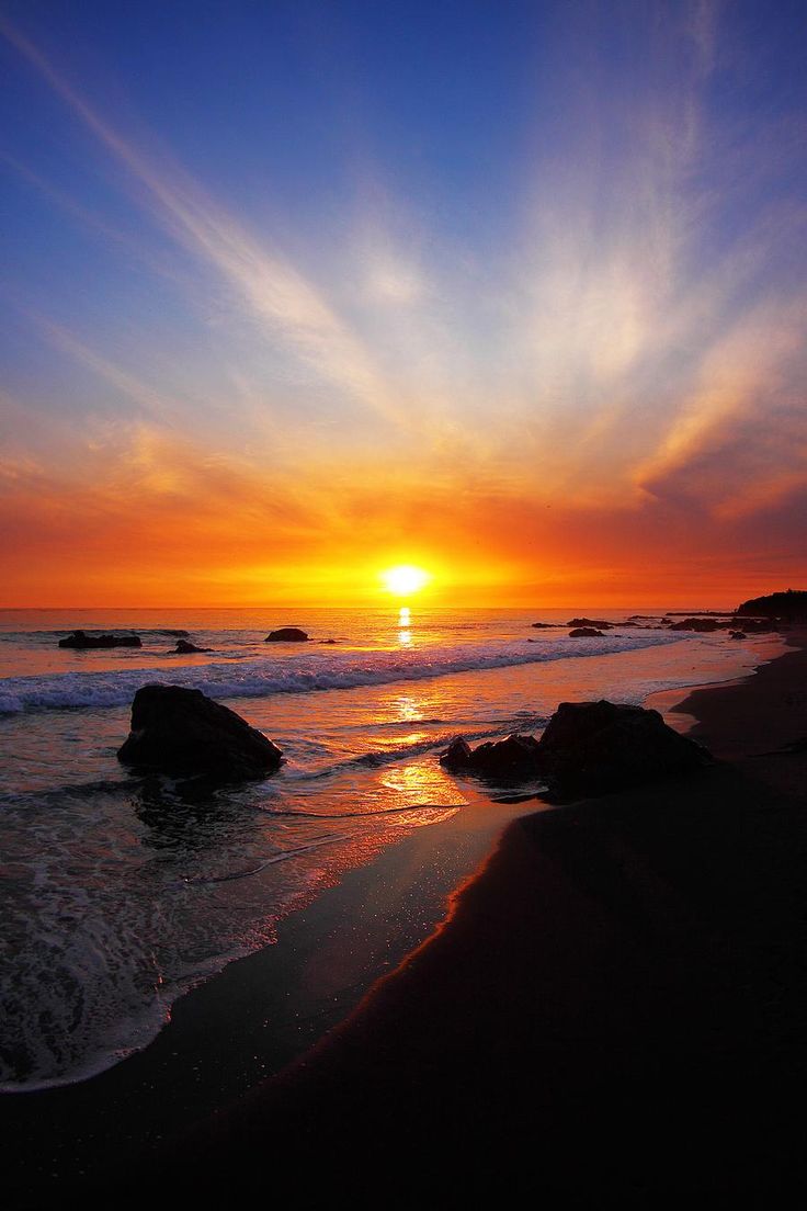 the sun is setting over the ocean with rocks