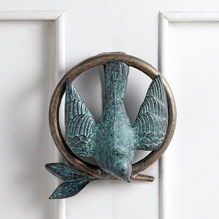 a metal bird mounted to the side of a white door with an open circle around it